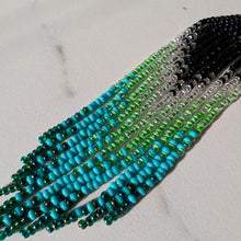Laden Sie das Bild in den Galerie-Viewer, A close-up of a beaded fringe earrings, strands transition from black at one end through clear and green beads to bright turquoise and dark teal at the other.
